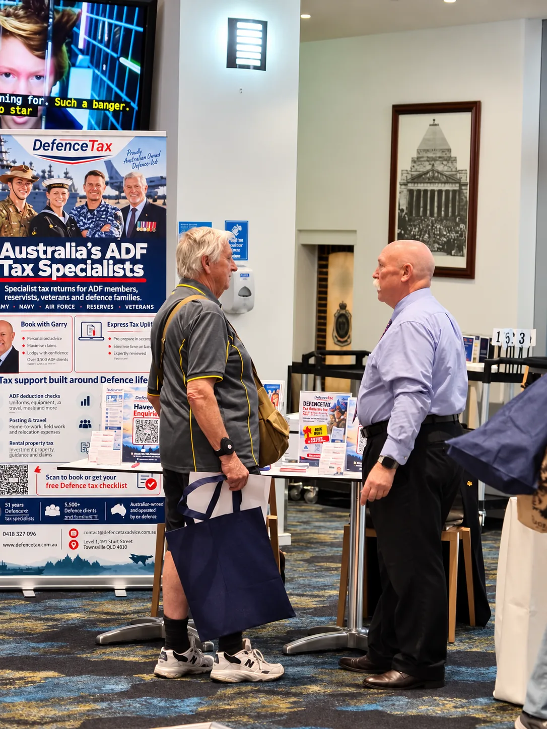 A DefenceTax representative speaking with a visitor beside the expo stand